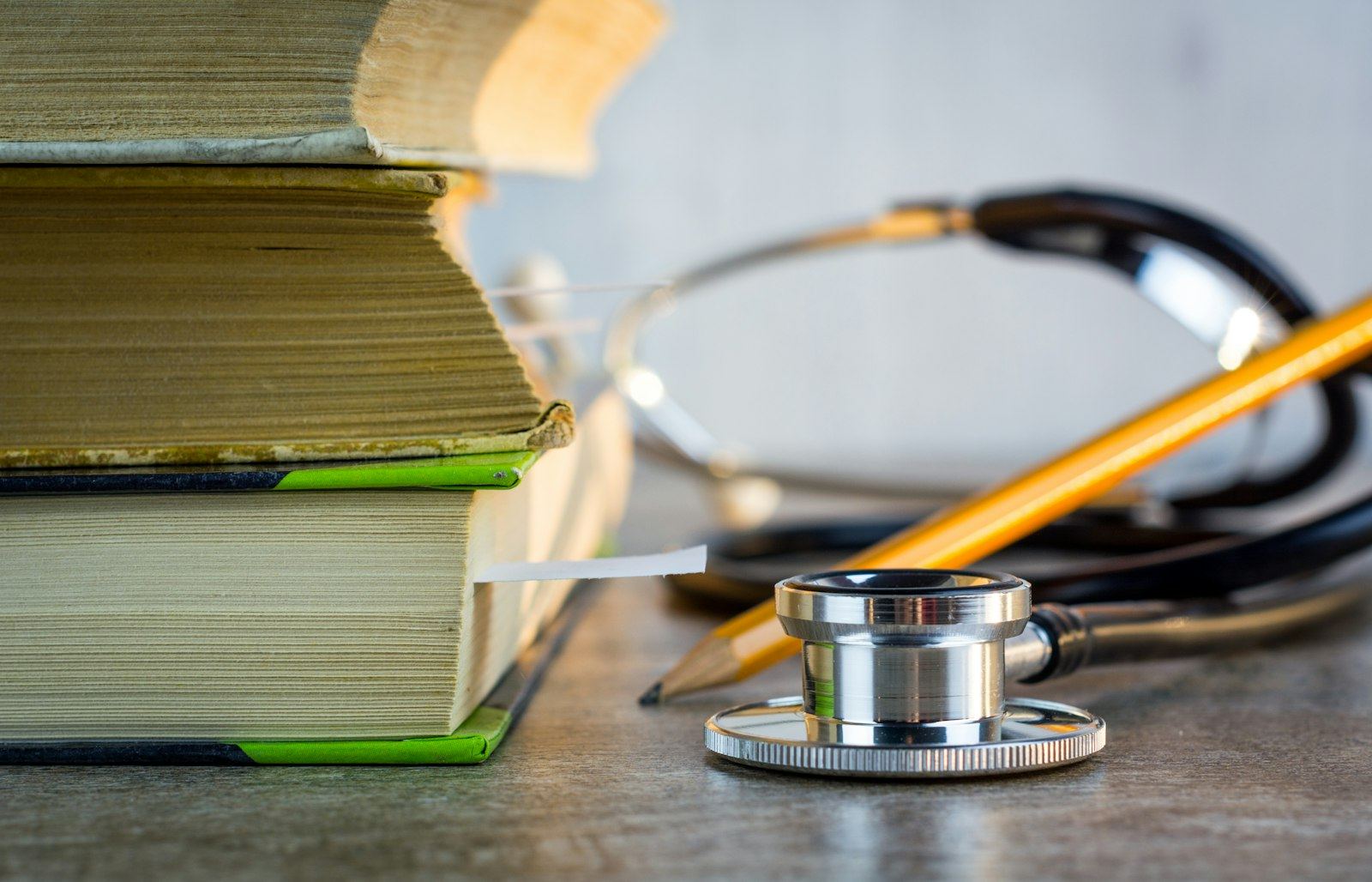 A stethoscope and pencil beside a stack of medical textbooks