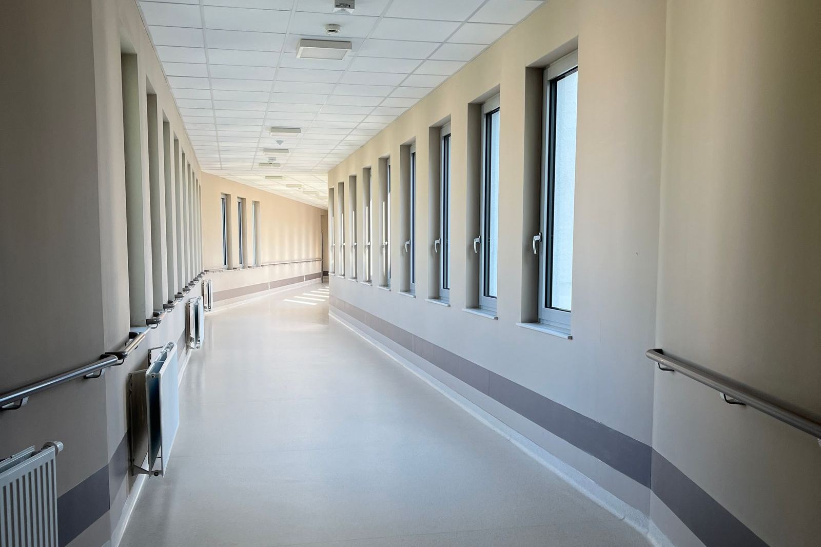 A long, bright hospital corridor with windows along one side
