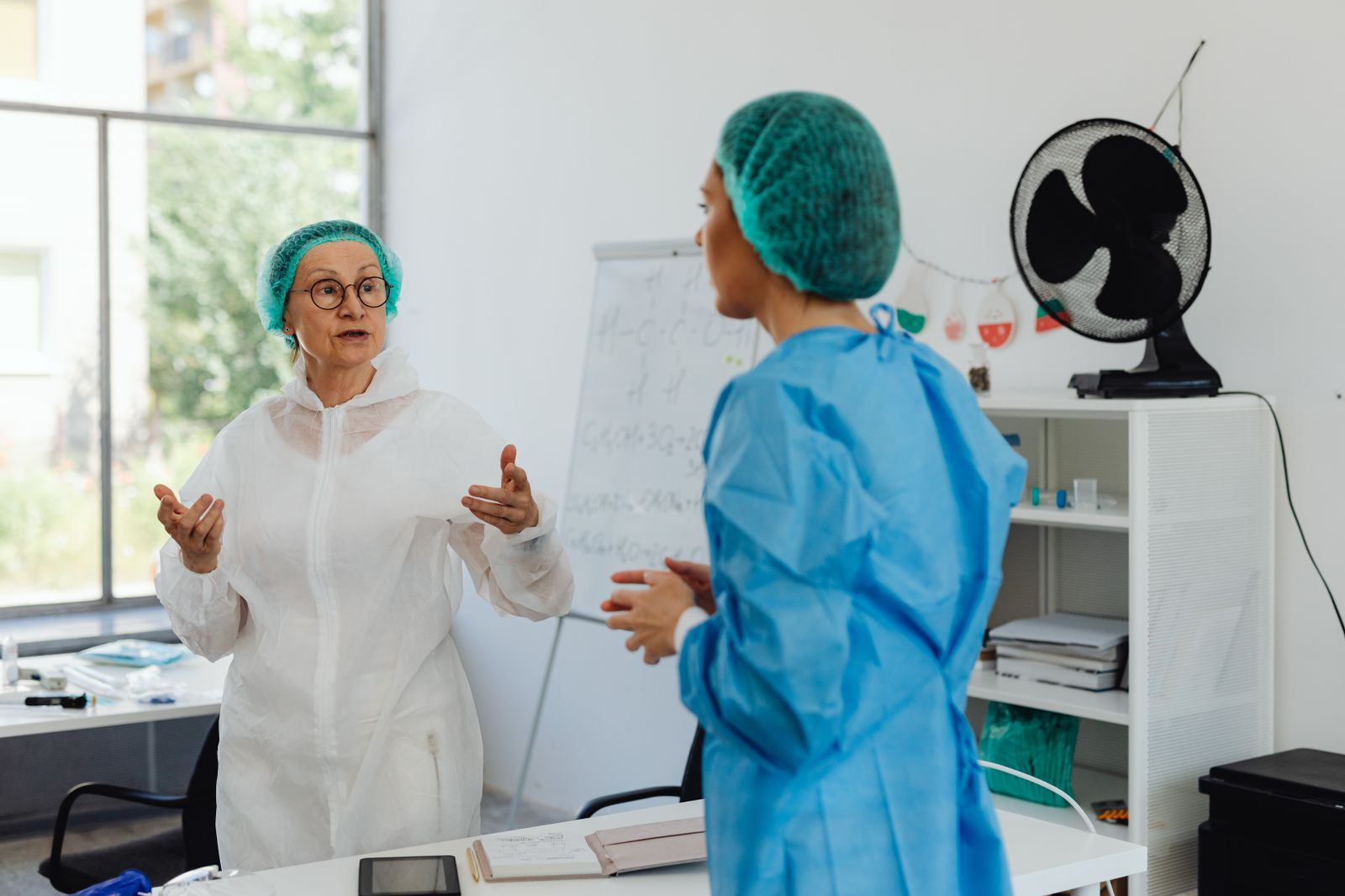 Two clinicians in scrubs talking in a bright office